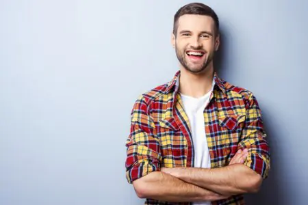 رجل مبتسم بقميص كاجوال يقف أمام جدار عيادة فاتح اللون