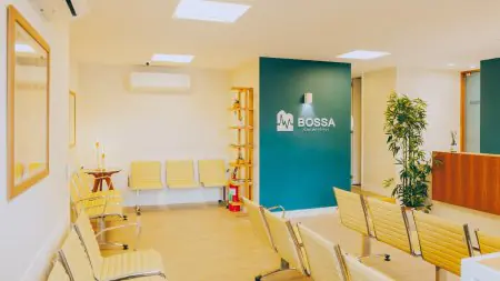 غرفة انتظار حديثة في عيادة Bossa Consultórios بكراسي صفراء ومكتب استقبال