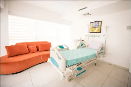 Habitación de paciente en Kyrenia IVF Center con cama hospitalaria y sofá naranja
