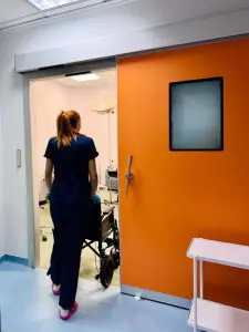 ممرضة مع كرسي متحرك تدخل غرفة المرضى في عيادة CorfuMedica