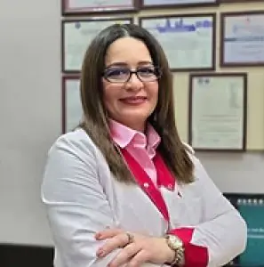 طبيبة في عيادة Şəfa MDM ترتدي معطفًا أبيض وخلفها شهادات معلقة