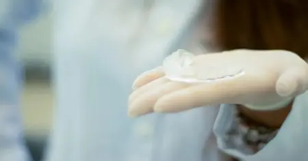 تقويم شفاف في يد مرتدية قفاز في عيادة Smile — Family Dentistry