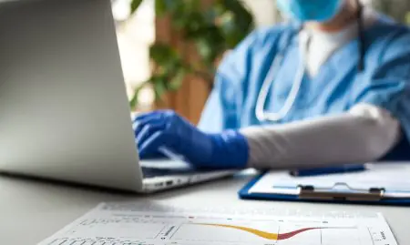 طبيب يرتدي زي طبي يعمل على كمبيوتر محمول مع مخططات طبية في مكتب العيادة