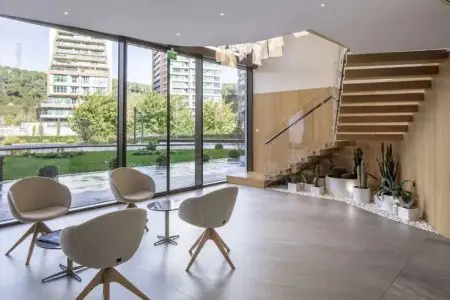 Sala de espera moderna en Qualident Dental Clinic con grandes ventanales y plantas
