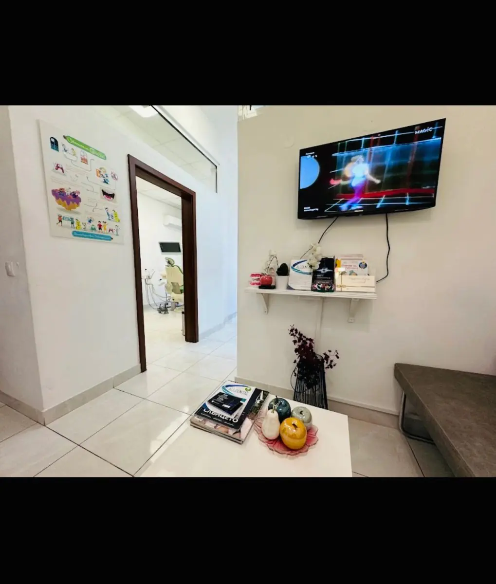 Salle d'attente de la clinique AllDental avec TV, magazines et vue sur la salle de soins dentaires