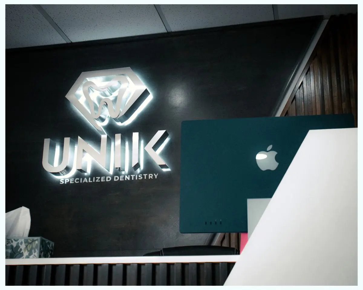 Reception desk at Unik Specialized Dentistry with modern decor and logo wall