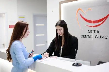مكتب استقبال في عيادة أسترا لطب الأسنان مع موظفة تساعد مريضًا