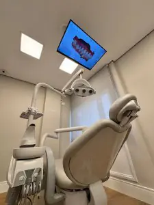 Sala de tratamiento dental con sillón moderno y pantalla en el techo en Kira Odontologia
